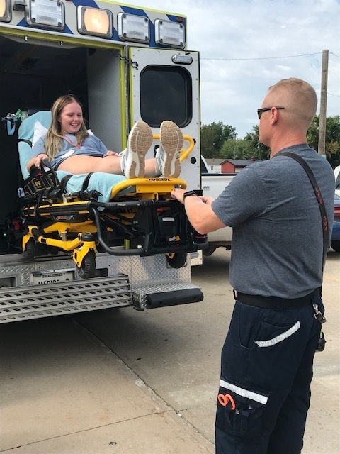 Health sciences student on medical gurney being put into ambulance to show how a person is transported during a medical emergency