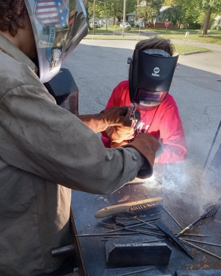 Welding student showing middle school student how to weld