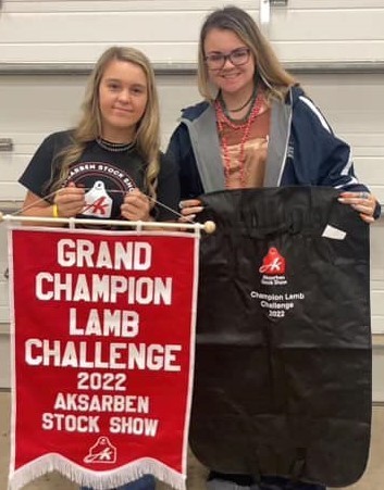 student and her sponsor posing with a grand champion lamb challenge banner from the Aksarben Stock Show